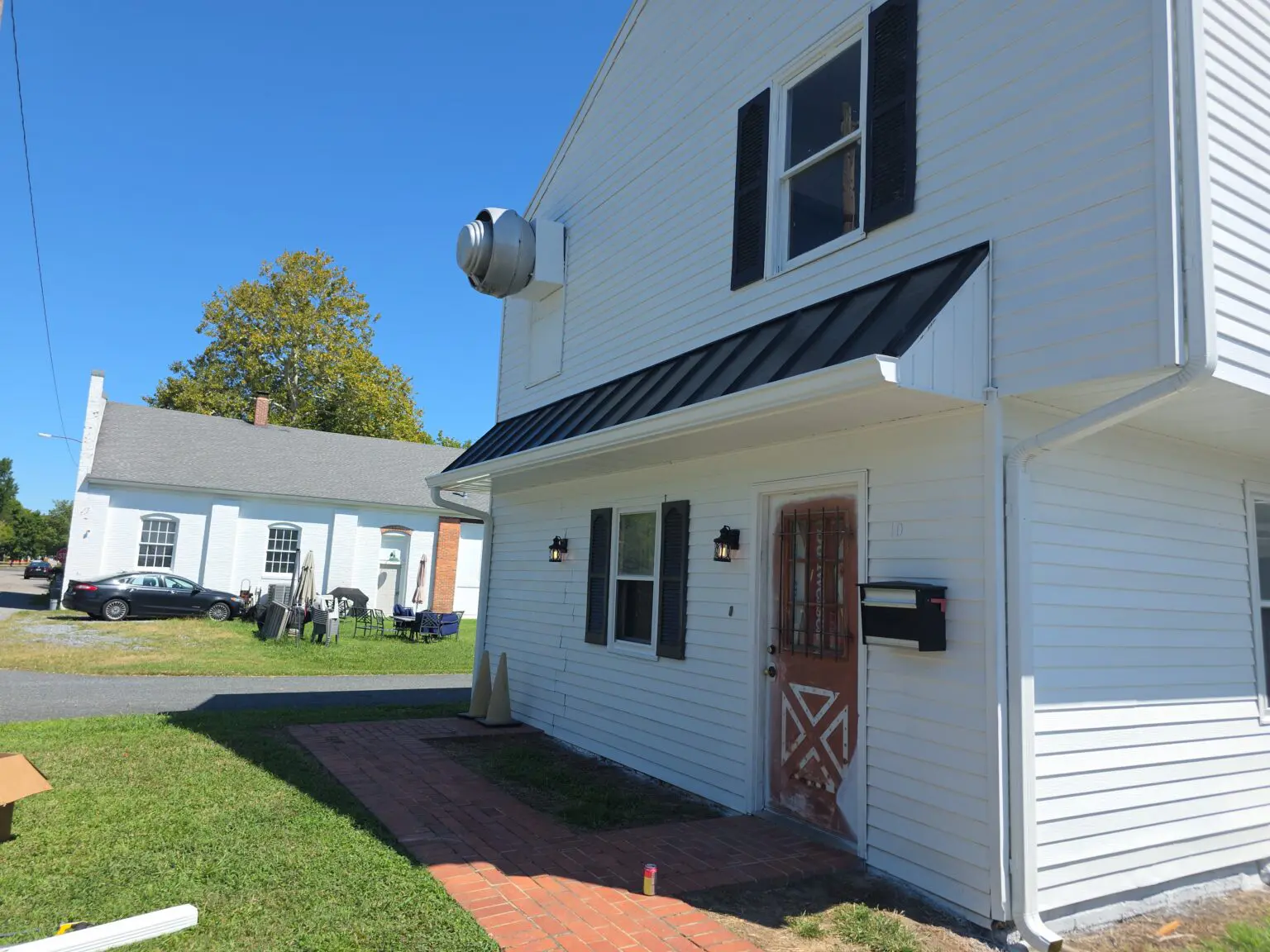 Side view of a building with fresh white horizontal siding, black shutters, and a sleek black metal awning over a red door with a white X-brace pattern.