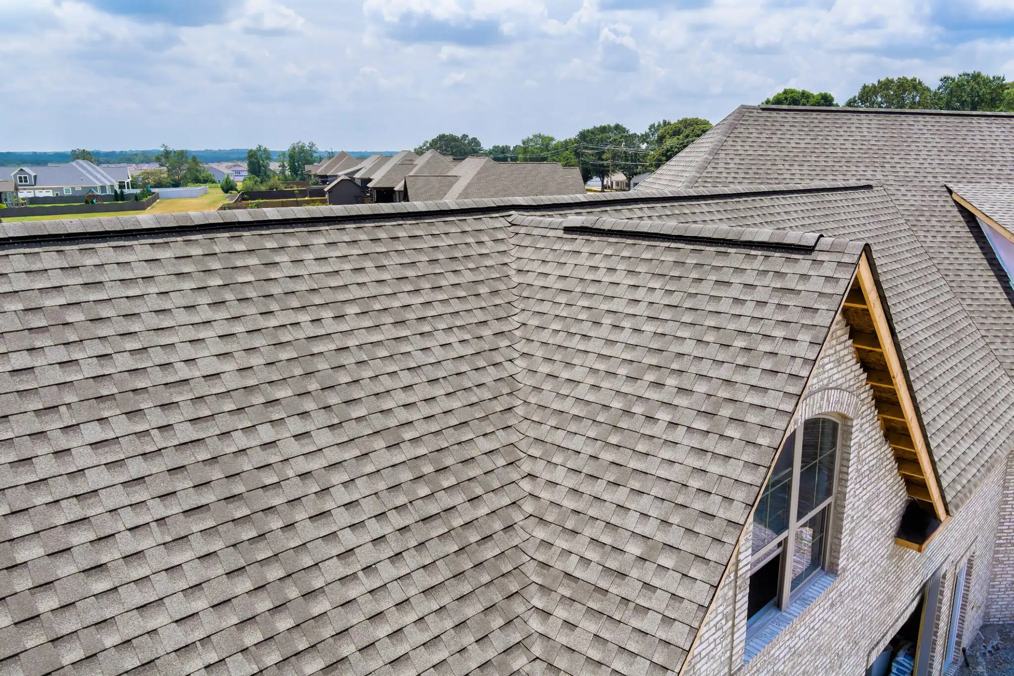 View new roofing on homes, surrounded by lush greenery under works area in suburban landscape.