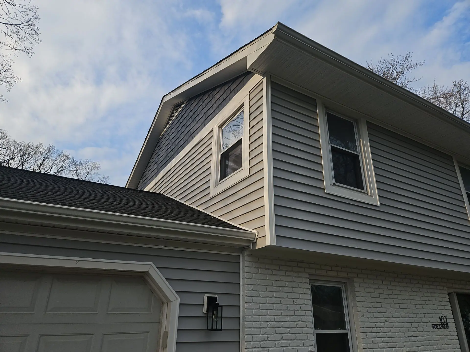Exterior view of a house showcasing gray siding, a gable roof, and multiple windows against a partly cloudy sky. Ideal for home design context.